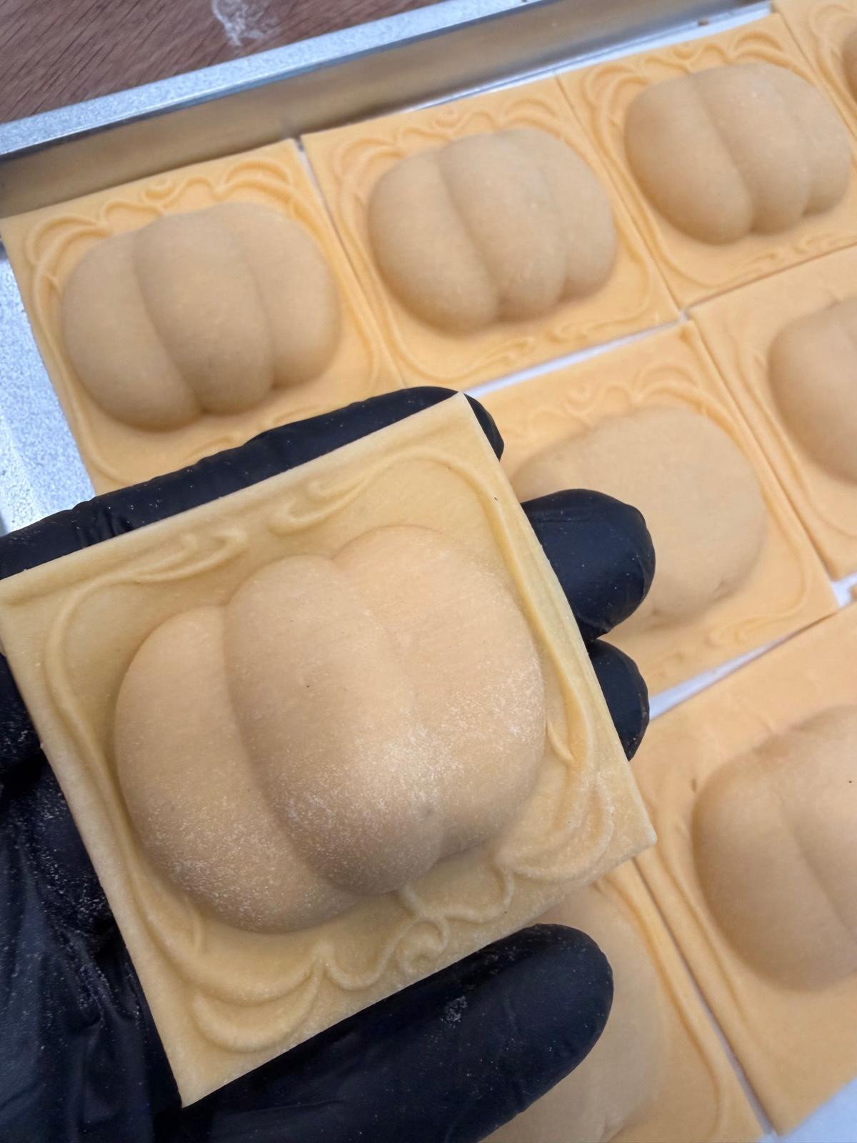 Fresh square ravioli held above a tray of handmade ravioli