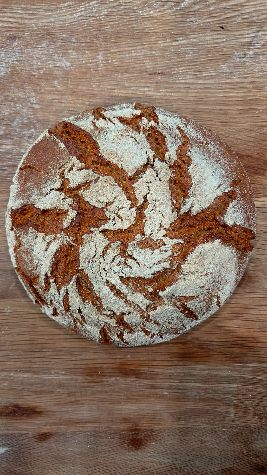 Round rye sourdough loaf with a flour-dusted, cracked crust on a wooden table